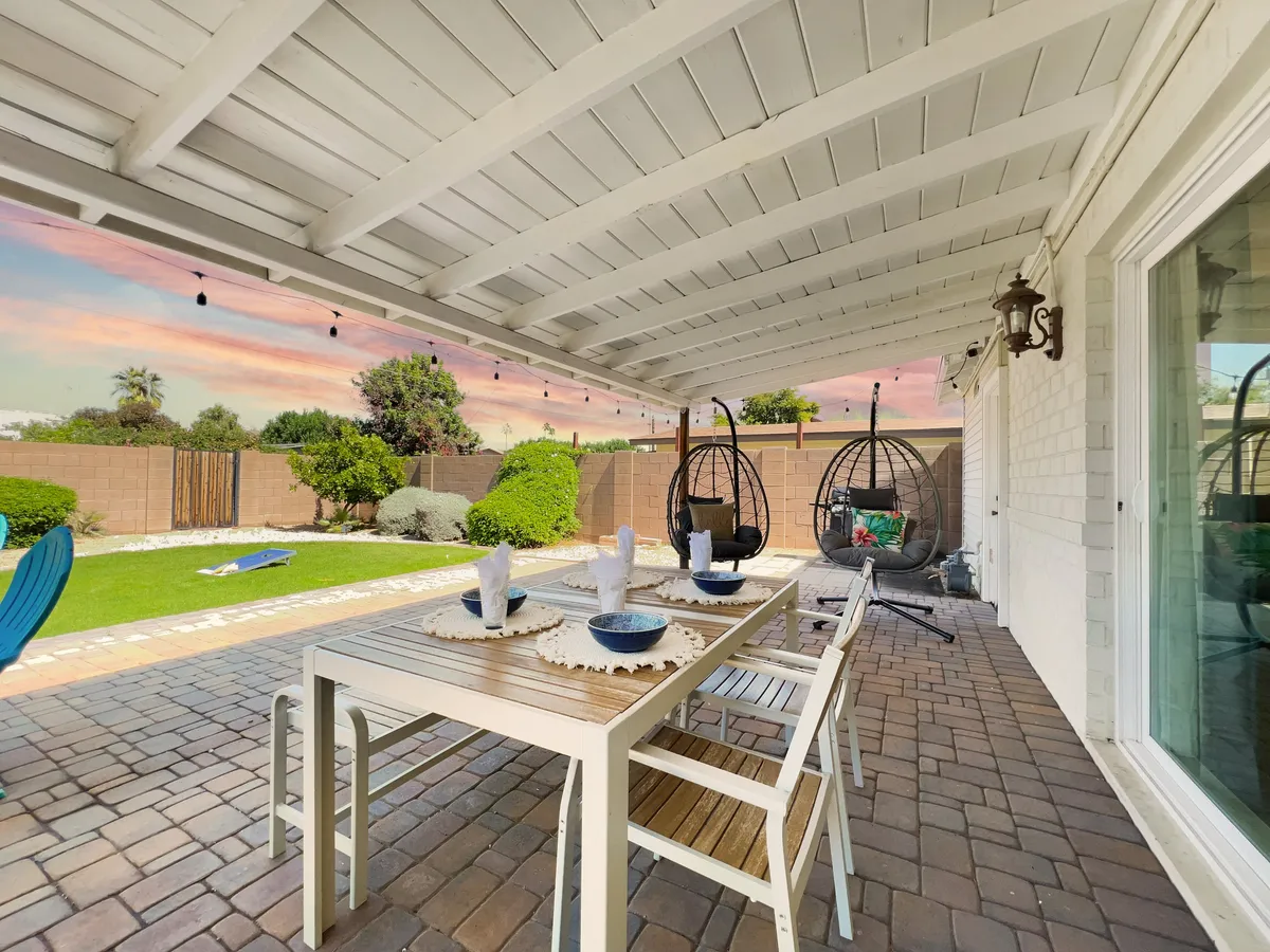 This image shows a charming outdoor dining area with a table set amidst a lush garden, complemented by hanging chairs that invite relaxation. The space is open, sunlit, and features clear pathways for gathering and enjoying the outdoors.
