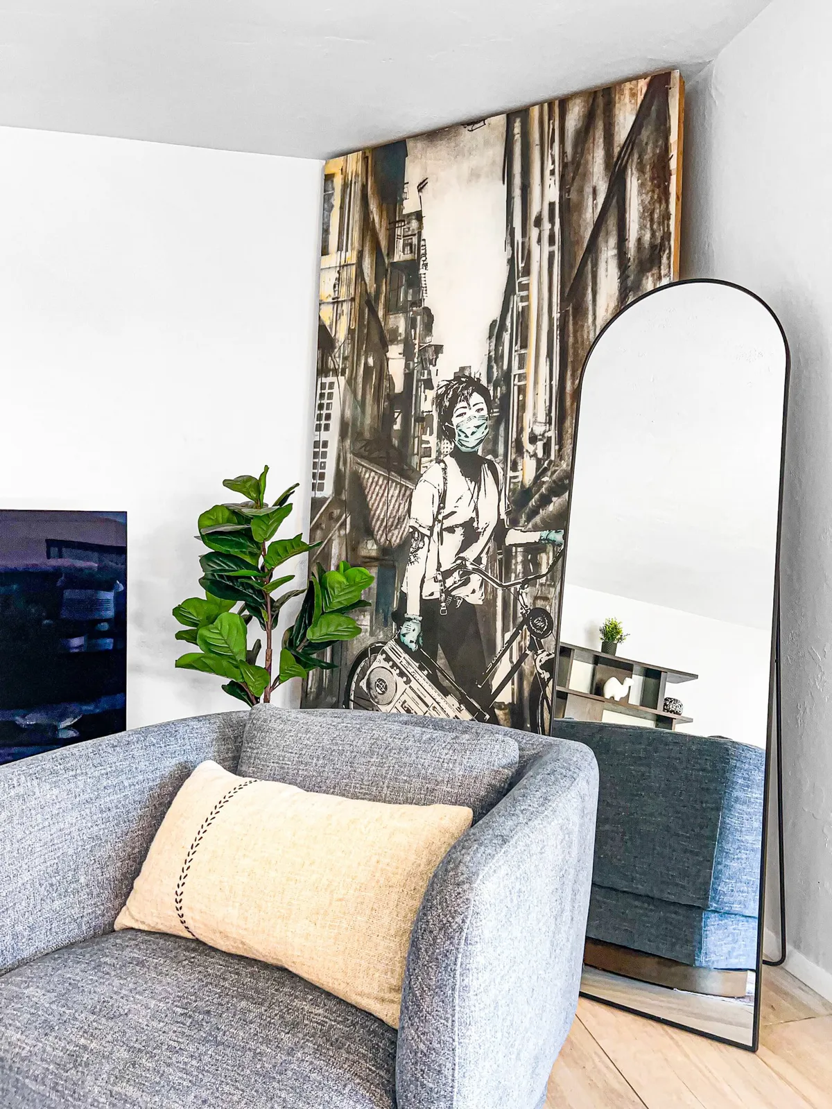 A stylish corner with a unique wall art centerpiece, a modern chair with a decorative pillow, a tall mirror that reflects natural light, and an indoor plant. The space feels contemporary, offering a spot for coffee breaks or contemplation.