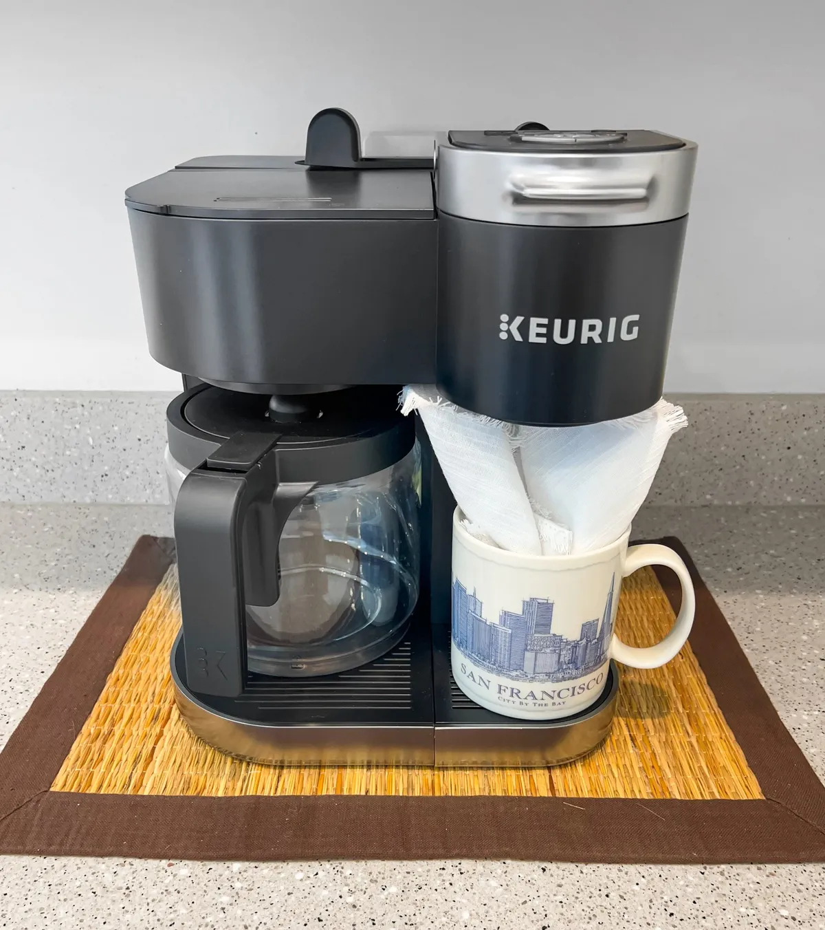 A cozy coffee station featuring a Keurig coffee maker, a glass coffee pot, and a mug sits on a kitchen counter. The setting radiates warmth and comfort, evoking morning routines and the pleasure of relaxing with a coffee before heading out.