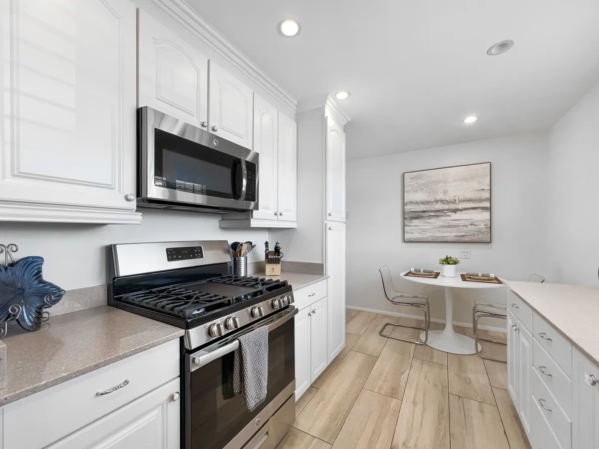 An open dining and kitchen area highlighted by stainless steel appliances, white cabinetry, and a stylish dining table with chairs. Warm lighting and artistic decor create an inviting atmosphere for enjoying meals with friends and family.