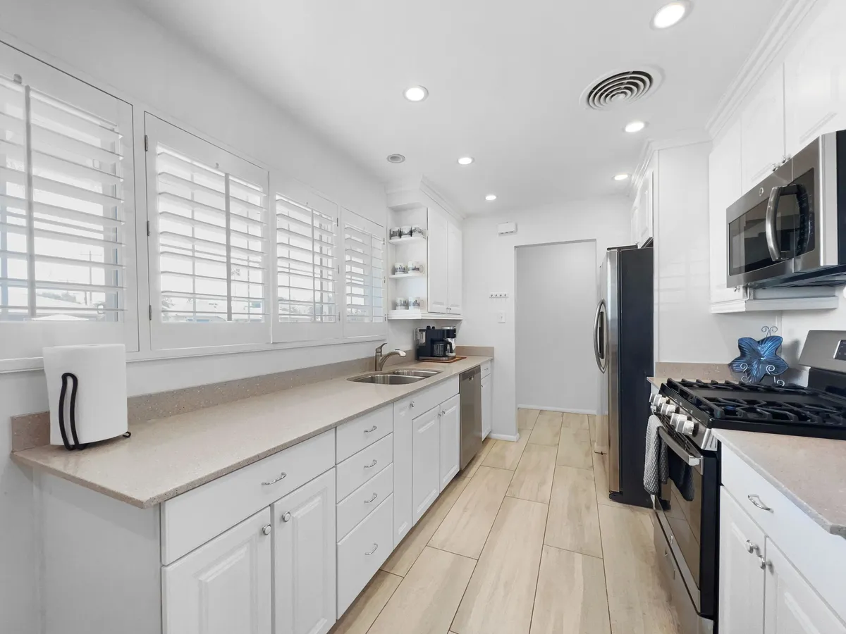 A bright, contemporary kitchen featuring sleek white cabinetry, shiny stainless steel appliances, and a spacious kitchen island perfect for meal preparation or entertaining. The setting conveys a sense of welcoming functionality, with enough room for cooking, gathering, and bringing home local ingredients.