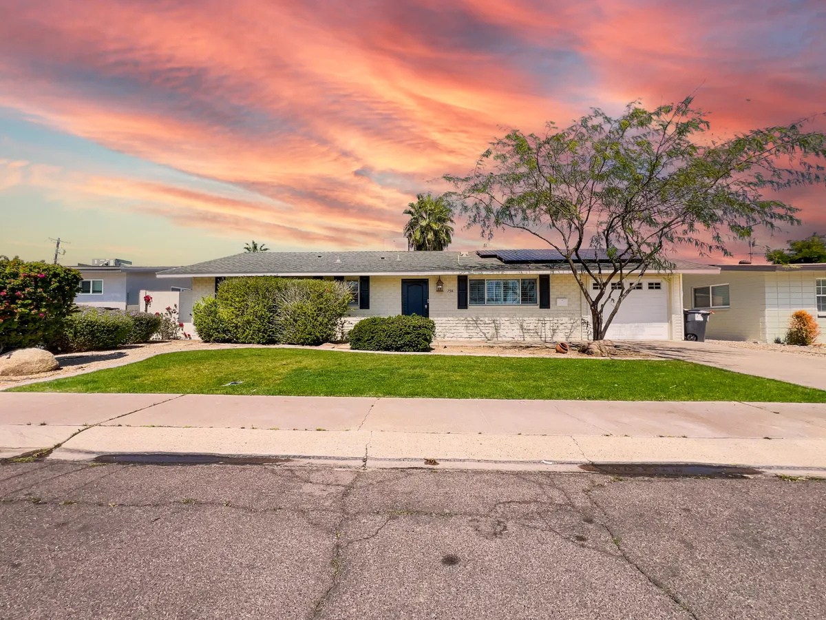 An inviting exterior shot of the house facade at sunset, featuring a lush green lawn, a prominent tree in front, and a welcoming porch. The tranquil and welcoming mood is enhanced by the vibrant sky and overall curb appeal.