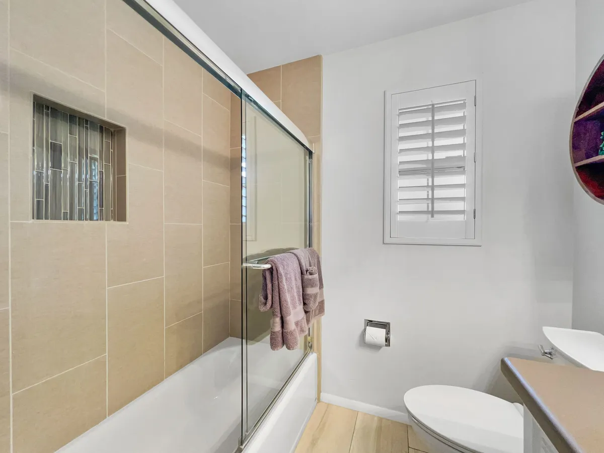 This inviting bathroom image shows a combination tub and shower, soft towels, and a window with shutters, blending functionality and style for comfortable self-care routines.