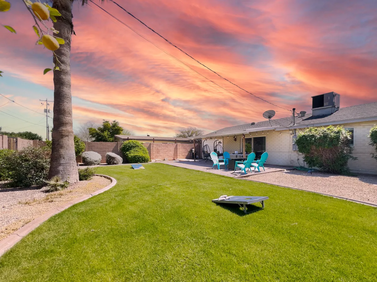 A large backyard with a lush green lawn and brightly colored chairs arranged for relaxation. The garden is bathed in the warm glow of a sunset, providing a peaceful, open space perfect for gatherings and play.